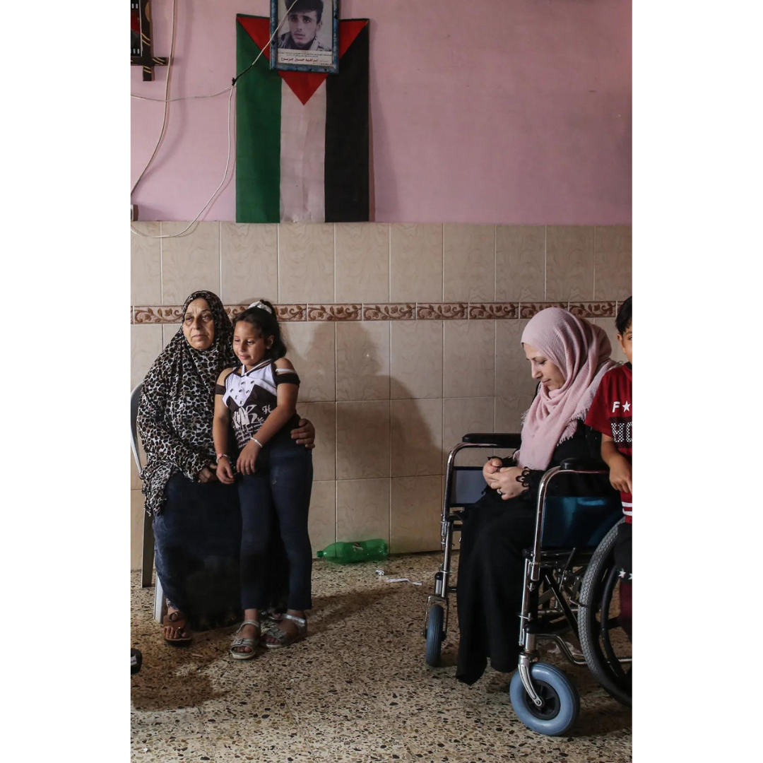 The picture shows two women, one sitting on a chair and the other sitting on a wheelchair. The picture shows the deterioration of the situation of women in Gaza after the war.